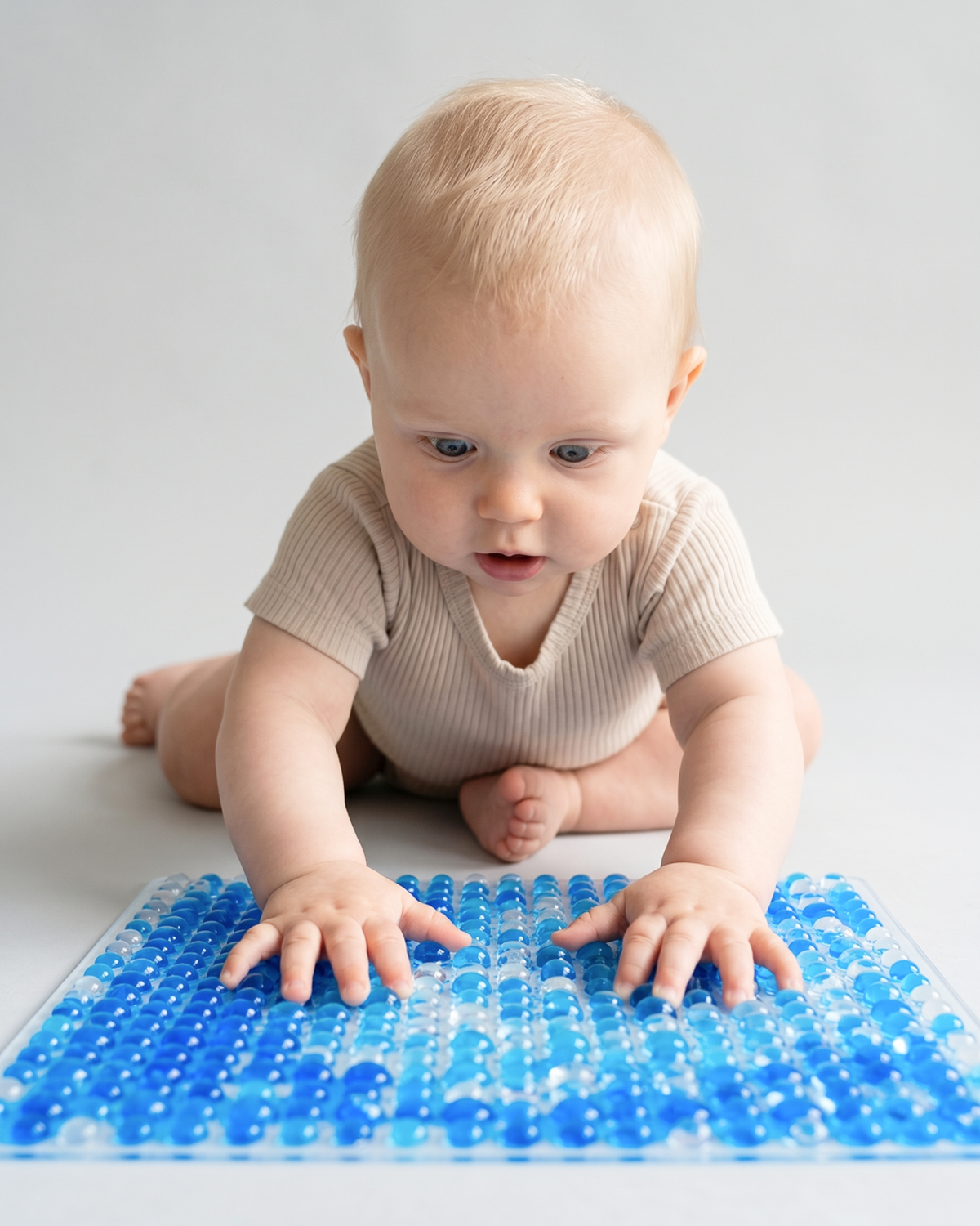 Baby trykker hænderne ned i den blå TUMLE SANSEMÅTTE™ med knopper