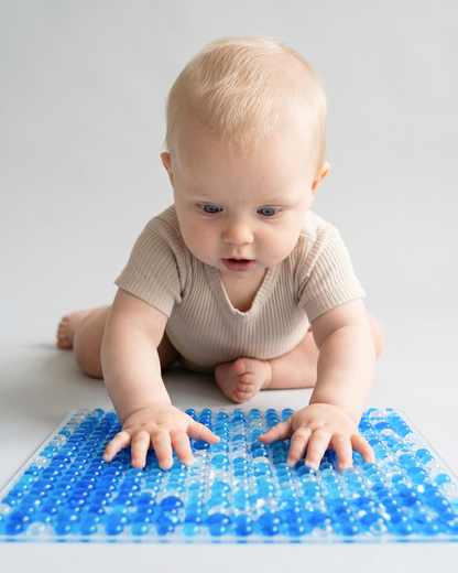 Baby trykker hænderne ned i den blå TUMLE SANSEMÅTTE™ med knopper